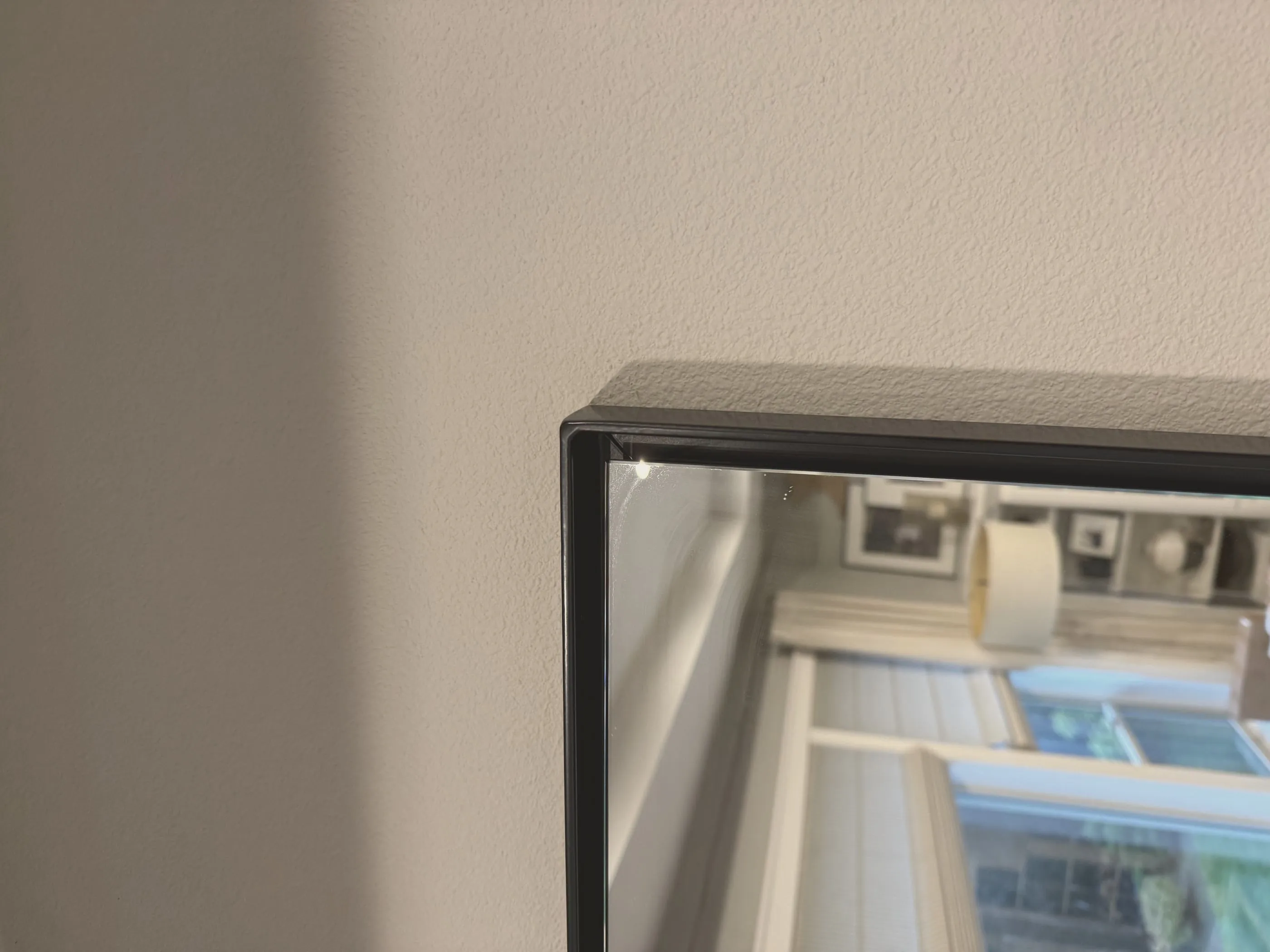 Close-up of a mitered corner on a black powder-coated steel frame, the glass sitting recessed behind the steel.