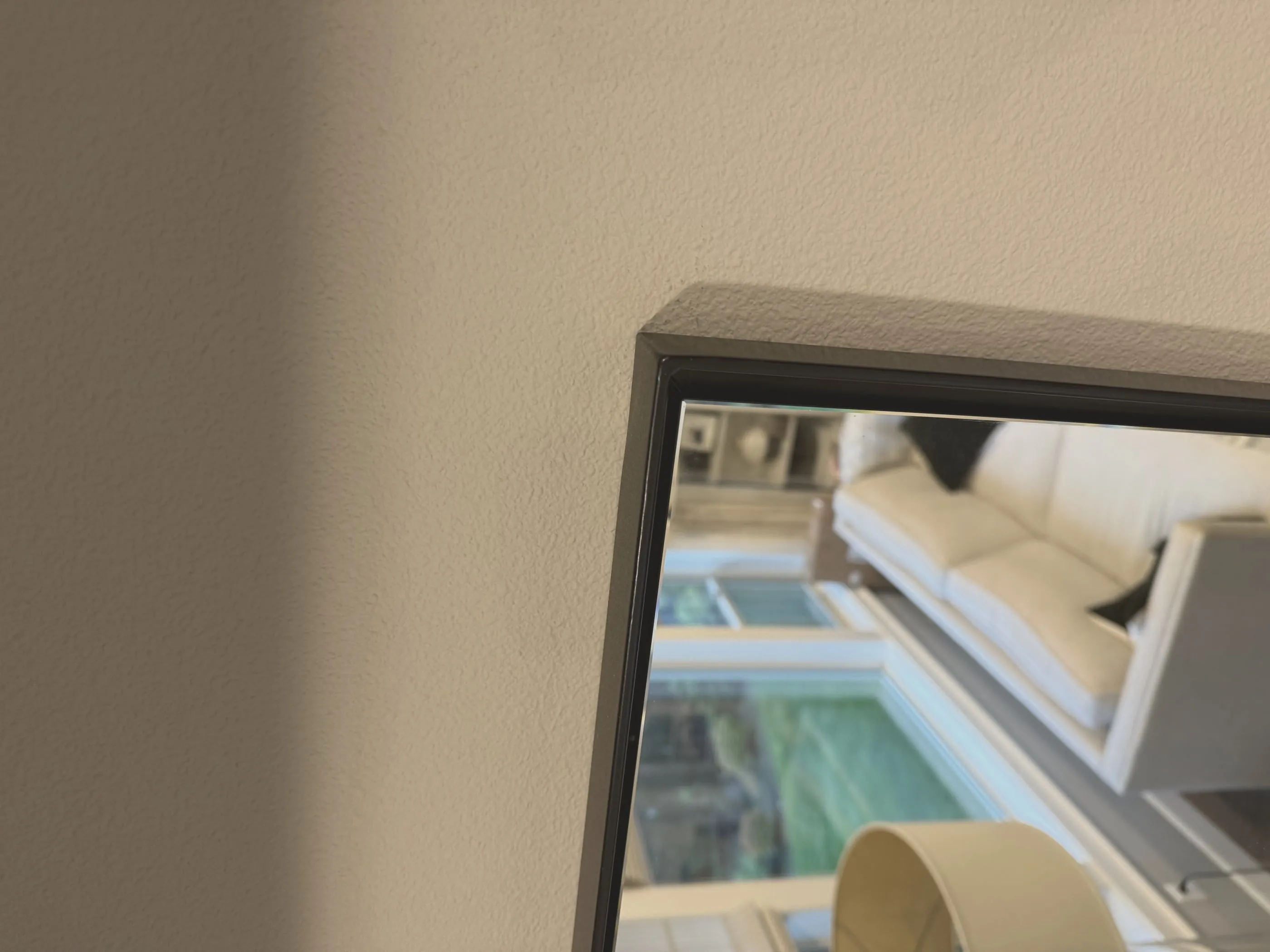 Macro detail of a mitered corner on a matte black powder-coated steel angle frame, showing the ground-flush joint and the glass recessed behind the steel.